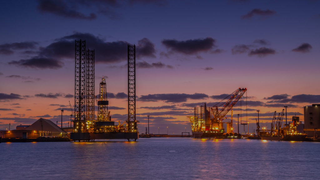 oil rigs and crane facilities on the ocean in the sunset