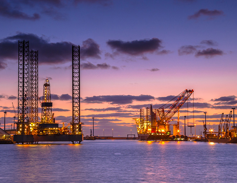 oil rigs and crane facilities on the ocean in the sunset